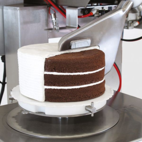 Maschine streicht weiße Creme gleichmäßig um eine Schokoladentorte